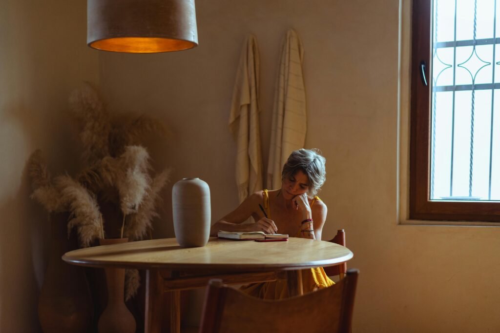 A senior woman enjoys journaling at a table in a warm, cozy home setting. Feeling the main character energy.